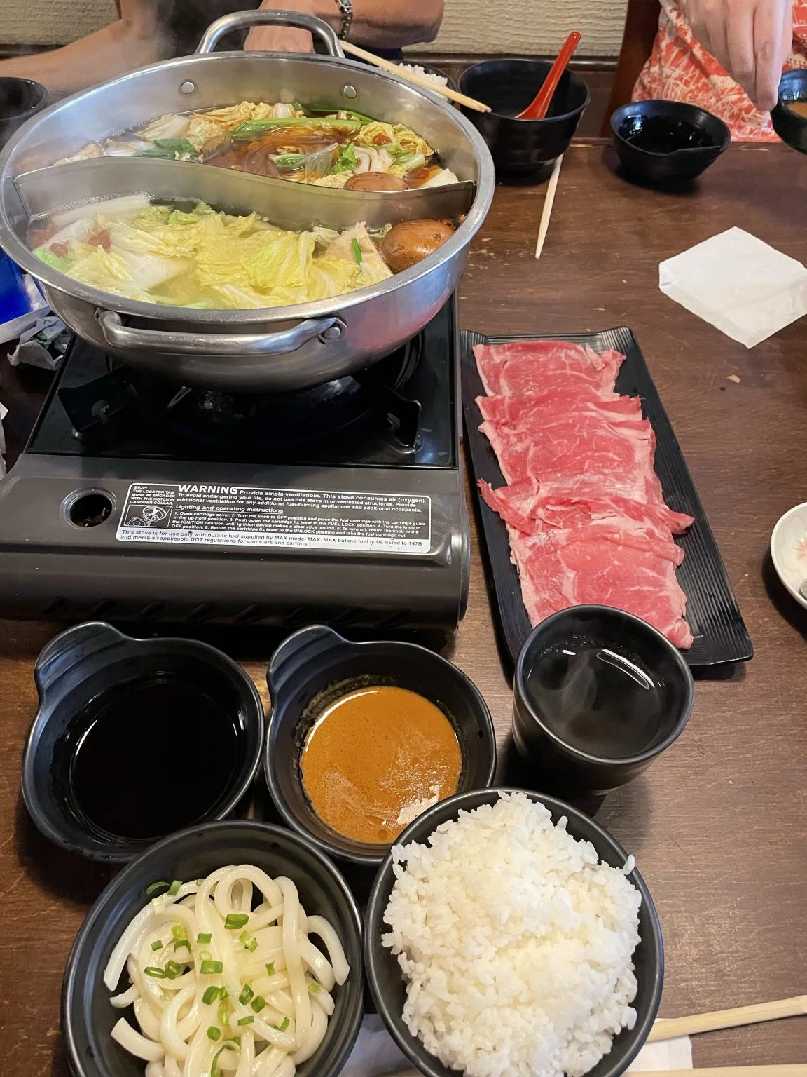 鍋と牛肉、うどん、ご飯が並ぶ食卓