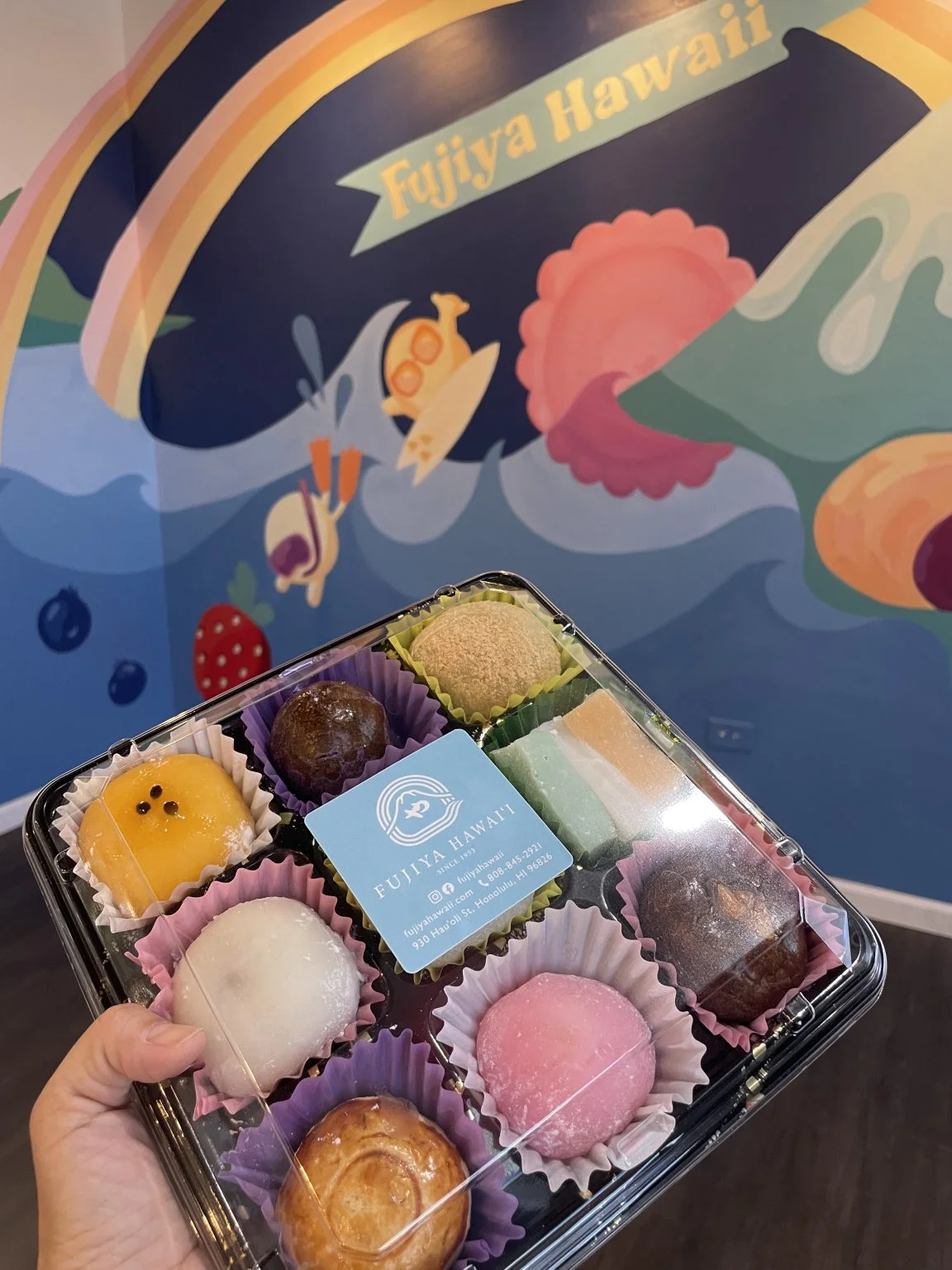 Fujiya Hawaiiの壁画の前で持つ和菓子の詰め合わせ