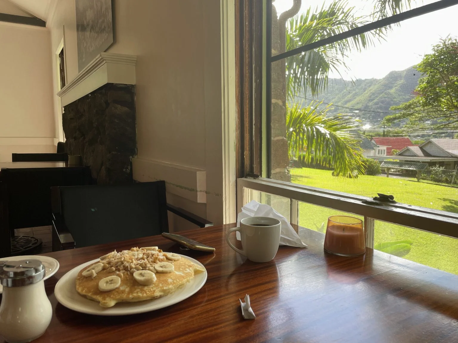 窓際の席に置かれたバナナパンケーキとコーヒー、山の景色