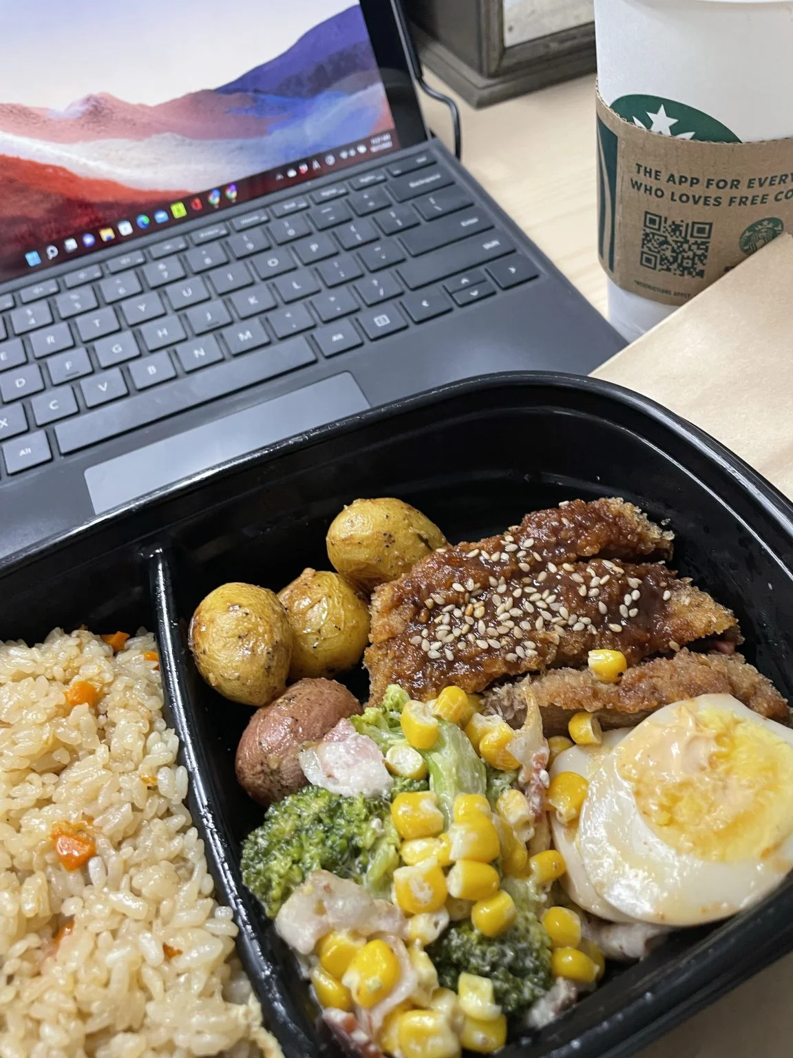 ノートパソコンの横に置いた玄米と惣菜のランチボックス