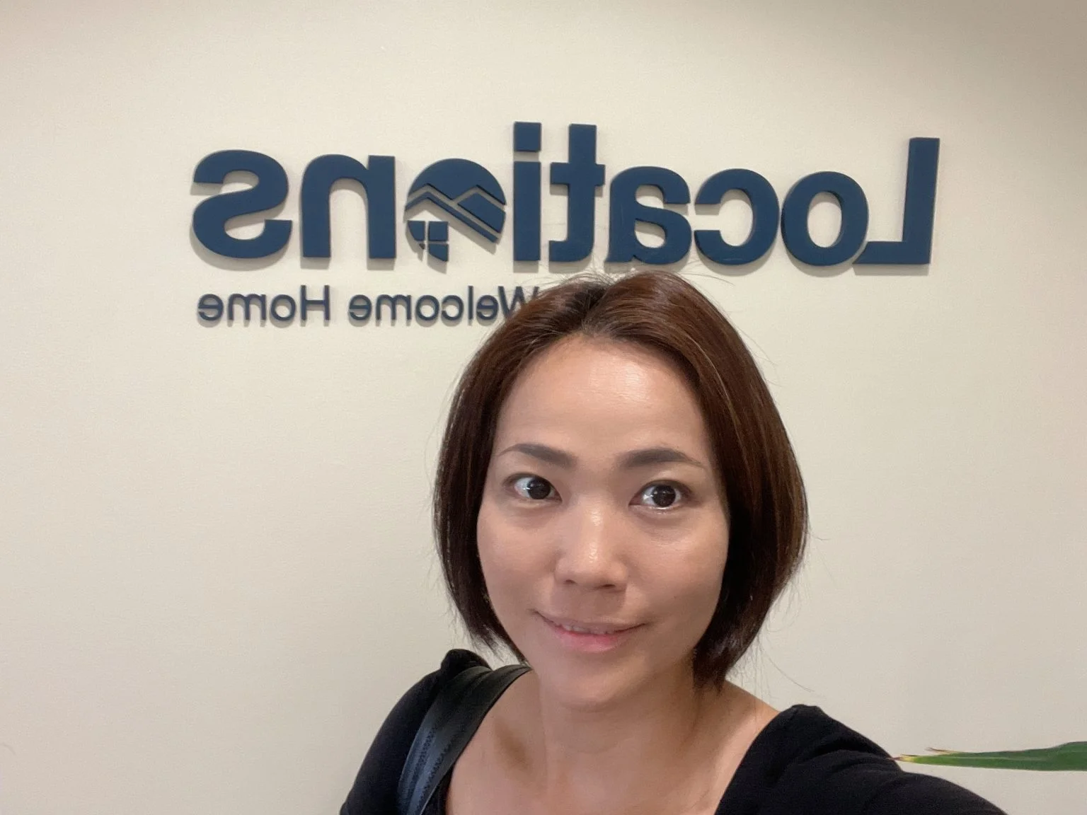 不動産会社のロゴ看板の前で自撮りする女性